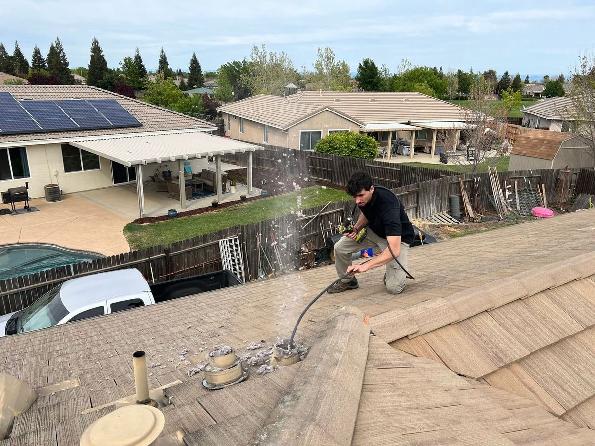Best Chimney LLC technician on a rooftop clearing a dryer vent with a rotary brush, lint blowing out of the roof vent