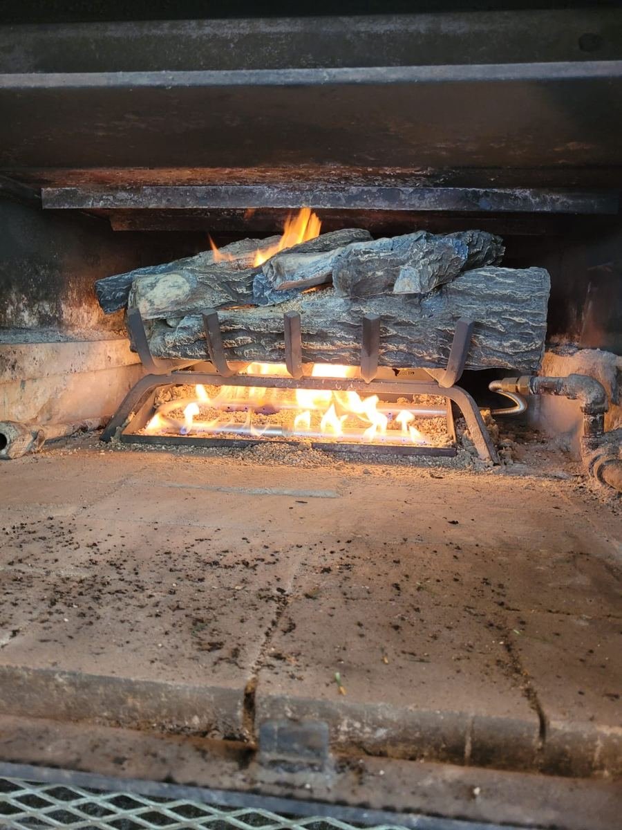 Lit gas log set burning evenly on a clean burner pan inside a serviced fireplace firebox